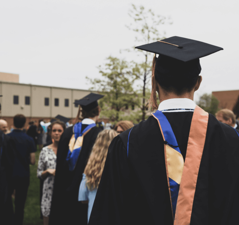 a graduation scene. several students appear in caps and gowns, standing alongside their families